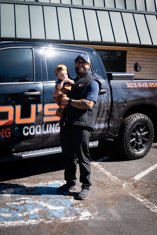 Lou Hernandez holding his young son in front of the Lou's Heating & Cooling service truck