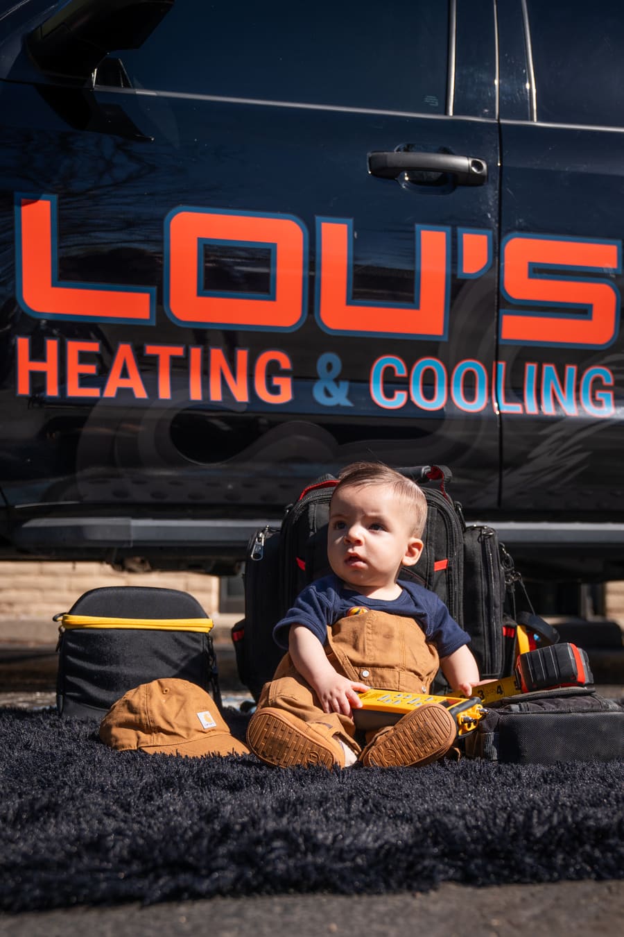 Lou's young son sitting with the tool bags in front of the Lou's Heating & Cooling truck